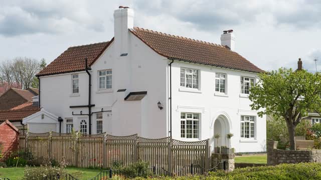 White two-story house with a red tiled roof, surrounded by a wooden fence and greenery in Burton Leonard, Yorkshire.