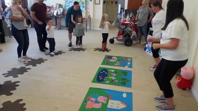 Children and adults participate in activities on colorful mats, with decorations and a playful atmosphere in a community center.