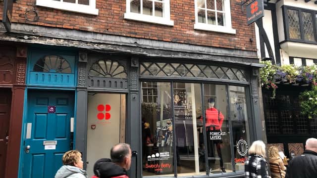 Sweaty Betty clothing store with large front window, red and black signage, and shoppers walking by in a quaint street.