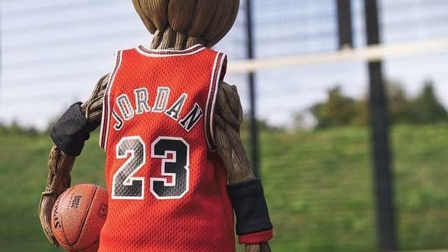 A small figure resembling a tree, wearing a red basketball jersey with "JORDAN 23," holding a basketball on a court.