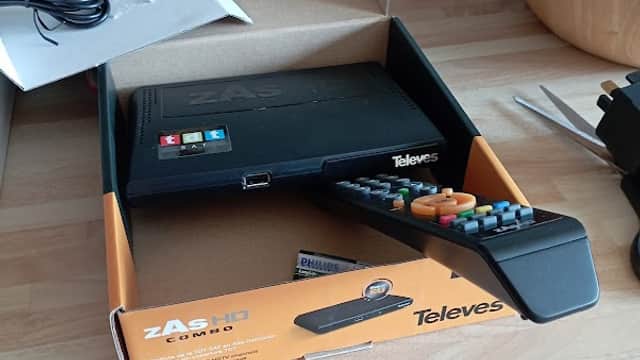 ZAS HD combo device in an open box with a remote control, on a wooden countertop with kitchen utensils in the background.