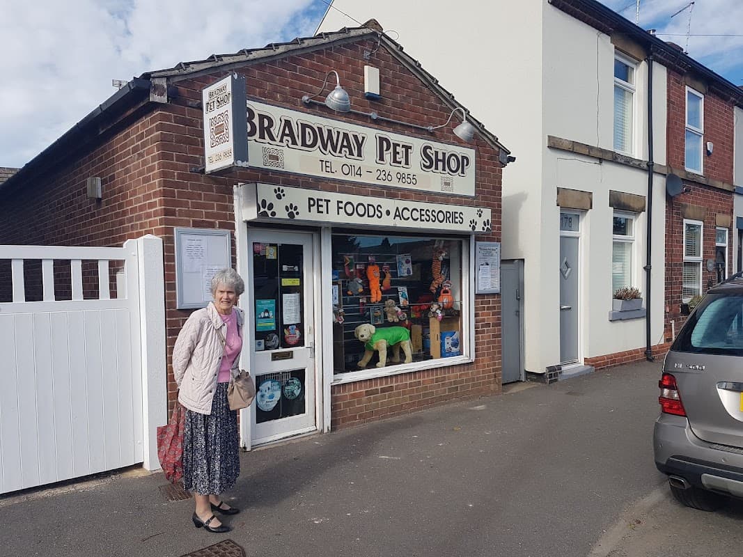 Exterior of Bradway Pet Shop with a woman standing outside, showcasing pet food and accessories in the window display.