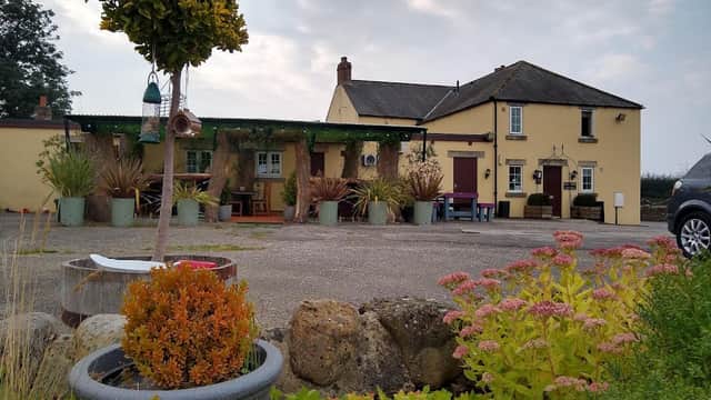 Yellow building of The Black-a-Moor Inn surrounded by greenery and colorful flowers, with a cloudy sky above.
