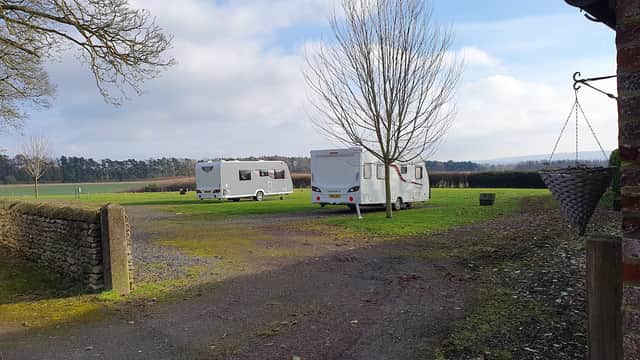 Two caravans parked on grassy area at Wykeham Grange Farm, surrounded by trees and open fields under a cloudy sky.