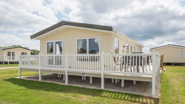 Modern holiday home with a spacious deck, surrounded by green grass and cloudy skies at South Cliff Holiday Park.