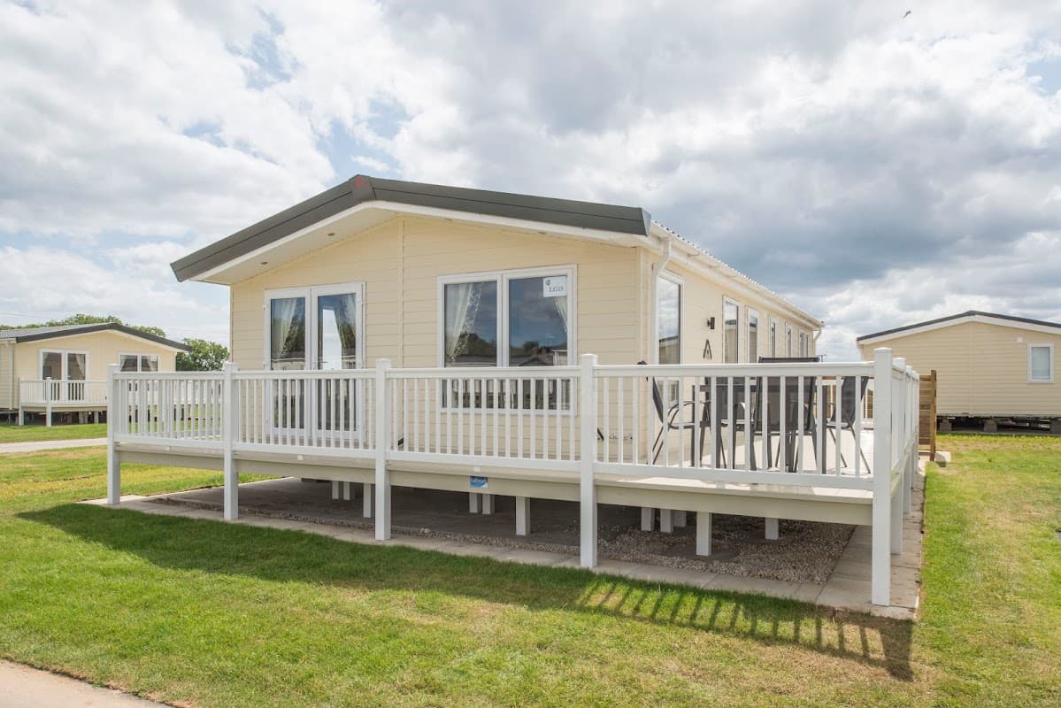 Modern holiday home with a spacious deck, surrounded by green grass and cloudy skies at South Cliff Holiday Park.