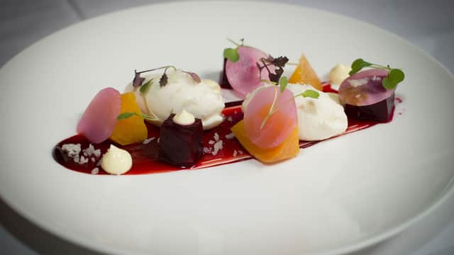 Elegant dish with colorful beetroot, dollops of cream, and microgreens on a white plate, arranged artistically.