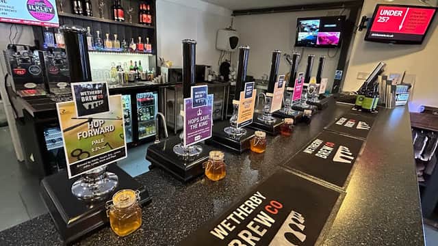 Bar counter with taps, various beer labels, jars of honey, and a selection of drinks in the background.
