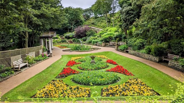 Lush garden with vibrant flowerbeds, pathways, benches, and greenery under a cloudy sky in Spa Bridge, Yorkshire.