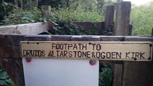 Signpost directing to footpath for Druids Altarstone and Ogden Kirk, surrounded by greenery and wooden fencing.