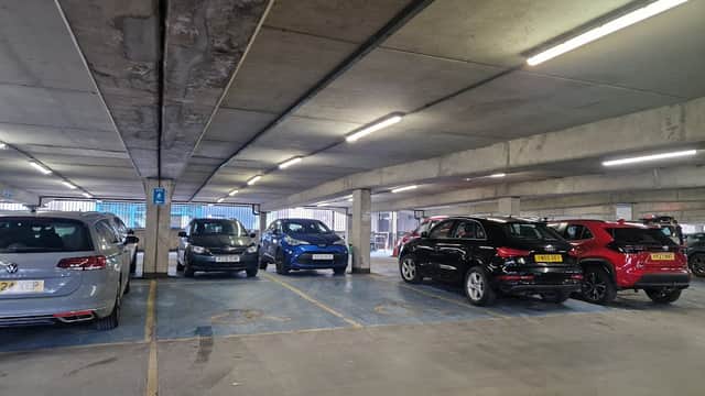 Cars parked in a multi-level car park with concrete walls and bright overhead lights.