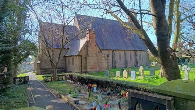 St. Michael Markington church surrounded by trees and a graveyard with flowers in Markington, Yorkshire.