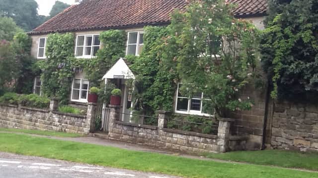 Charming stone cottages with a red-tiled roof, surrounded by greenery and a stone wall, in a rural setting.