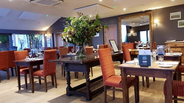 Cozy dining area with wooden tables, orange chairs, and a large floral arrangement in the center. Warm, inviting ambiance.