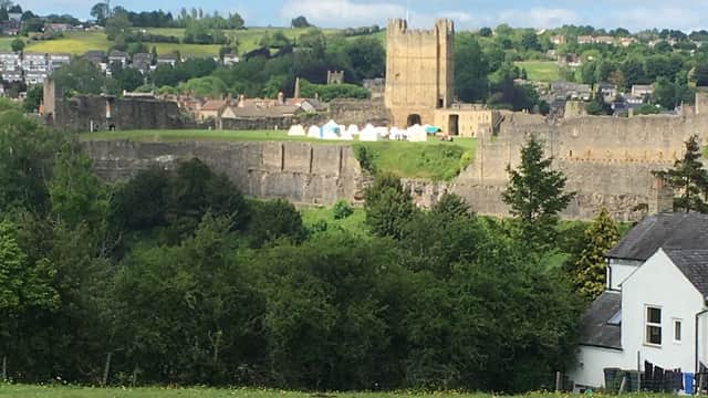 Scar Close Caravan Park with green fields, white tents, and a historic castle tower in the background under a blue sky.