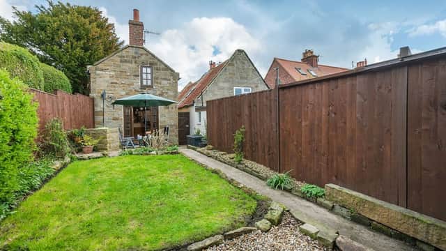 Charming stone cottage with a green lawn, patio furniture, and wooden fencing in a peaceful garden setting.