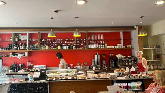 Bright coffee shop interior with a red wall, glass display of pastries, and two women chatting near the counter.