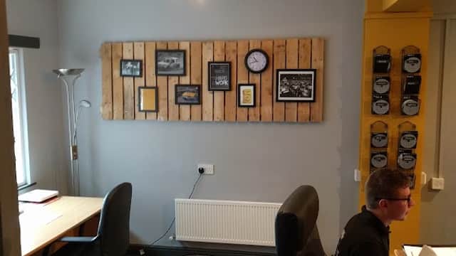Modern office space with wooden wall decor, a clock, two desks, and a cozy pet bed on the carpeted floor.