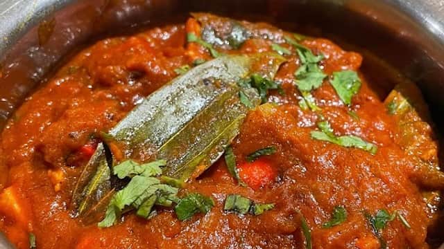 A rich, spicy curry topped with green herbs in a metal bowl, surrounded by other colorful dishes.