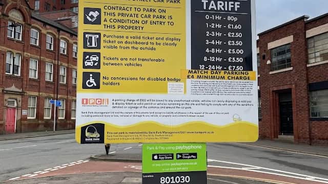 Sign for Arundel Street Car Park detailing parking tariffs and conditions, with nearby buildings in the background.