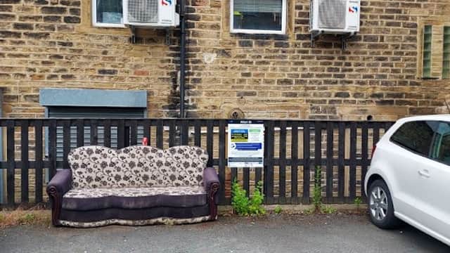 A parked white car beside a brown sofa with floral upholstery in front of a stone building with air conditioning units.
