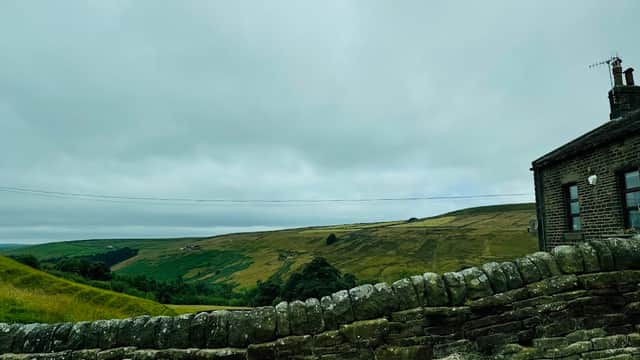 Stone wall in foreground with a view of rolling green hills and a cloudy sky in Cragg Vale, Yorkshire.
