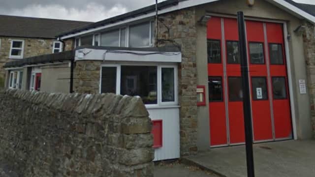Reeth Fire Station features stone walls, large red garage doors, and a white entrance, set against a cloudy sky.