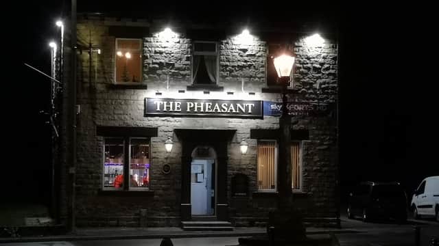 A stone pub with bright signage reading "The Pheasant," illuminated at night, featuring a lamppost nearby.