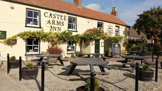 The Castle Arms Inn, a cozy bar with illuminated signage, outdoor seating, and lush greenery at night.
