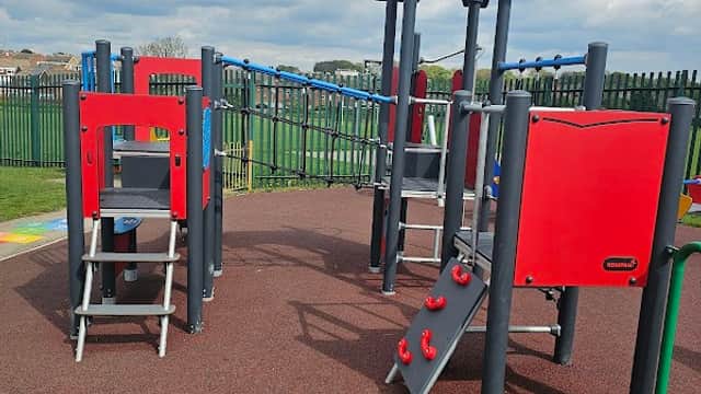 Colorful playground equipment with slides and climbing structures on a rubber surface under a partly cloudy sky.