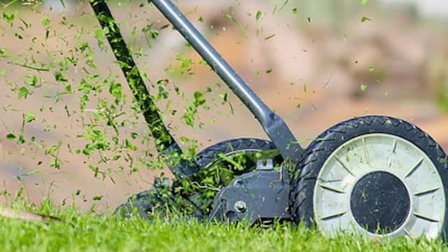 Lawnmower cutting grass, with clippings flying in the air, set against a green lawn background.