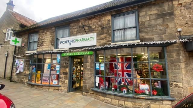 Stone building with large windows, displaying festive decorations and a Union Jack flag, labeled "Pickering Pharmacy."