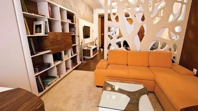 Modern living room with orange sectional sofa, white shelving, and decorative wall design. Stylish and contemporary decor.