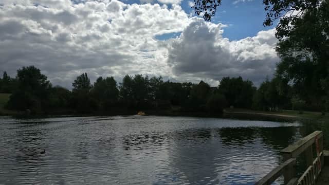 Calm water reflects clouds and trees at Hemsworth Water Park, with a wooden fence in the foreground.