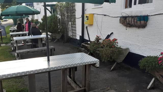 Outdoor seating with wooden tables and green umbrellas, surrounded by potted plants at The Gait Inn in Millington.