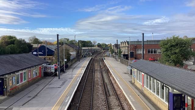 Railway tracks converge at Guiseley station, flanked by platforms and buildings under a blue sky with scattered clouds.