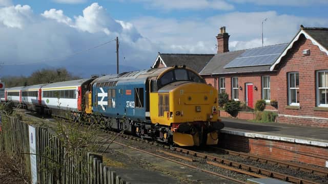 Train at Battersby station with a red-brick building and solar panels under a partly cloudy sky.