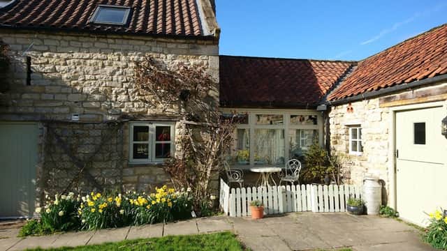 Charming stone cottages with a garden, white picket fence, and blooming daffodils under a clear blue sky.