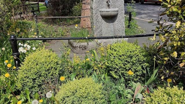 Granite memorial stone surrounded by lush greenery and colorful flowers in a quaint Yorkshire street.