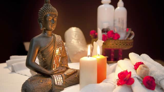 Buddha statue surrounded by candles, towels, and rose petals, creating a tranquil spa atmosphere.