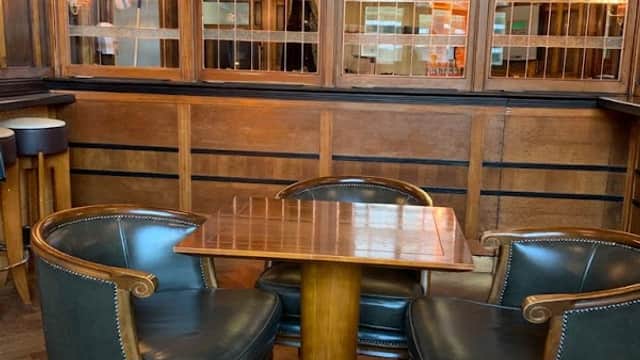 Wooden interior of "The Coach & Horses" pub, featuring a small table and leather chairs against a backdrop of glass panels.