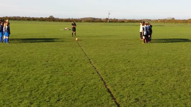 Two teams huddle on a grassy field, preparing for a match under a clear blue sky in Shipton-by-Beningbrough.
