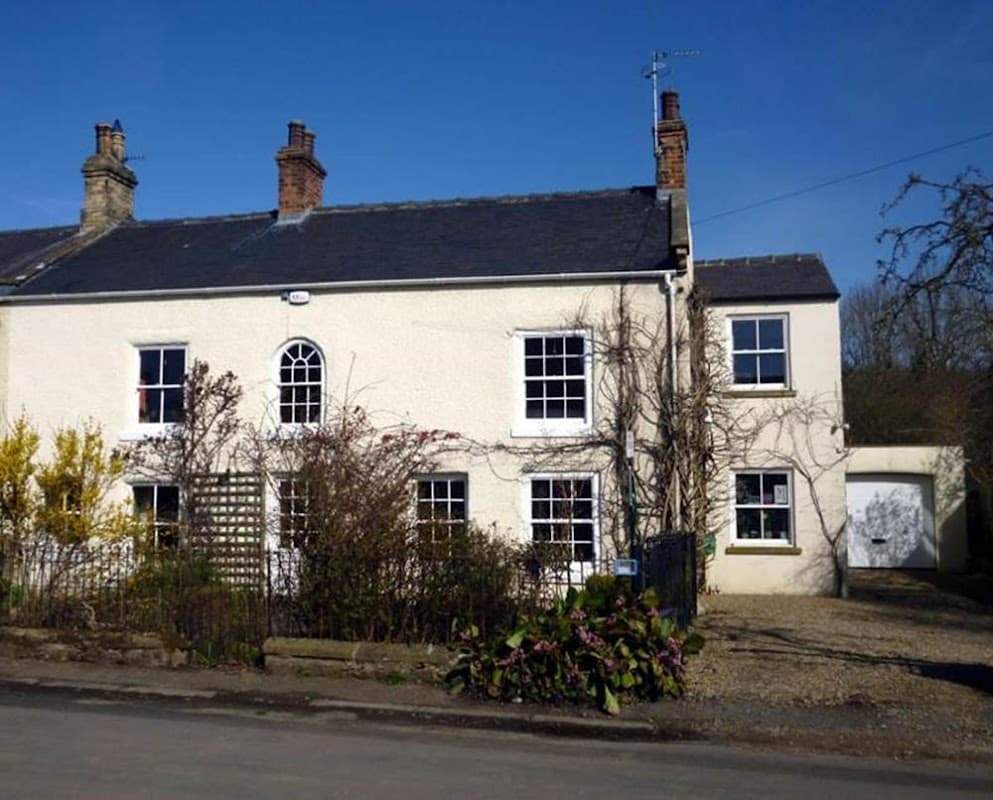 Charming white building with multiple windows, surrounded by greenery and a clear blue sky in Mickley, North Yorkshire.