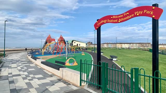 Colorful playground equipment with swings and climbing structures, surrounded by green grass and a scenic coastal view.