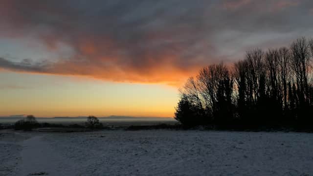 Sunset over snow-covered ground with silhouetted trees and a colorful sky at Richmond Racecourse.