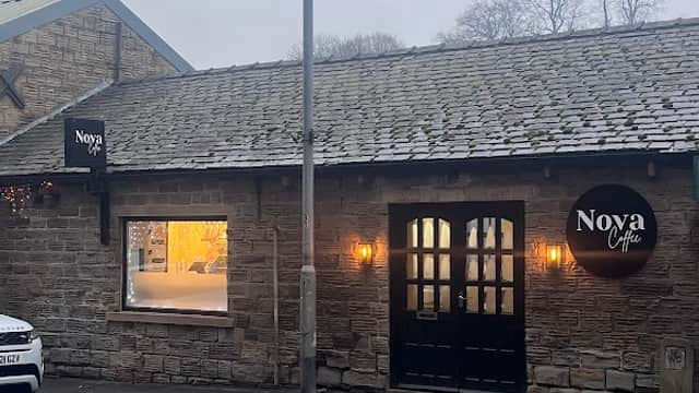 Stone building with a slate roof, featuring large windows, a wooden door, and "Nova Coffee" signage.