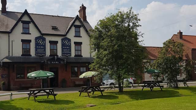 The Blue Bell Inn in Weaverthorpe, featuring outdoor seating and green umbrellas on a sunny day.