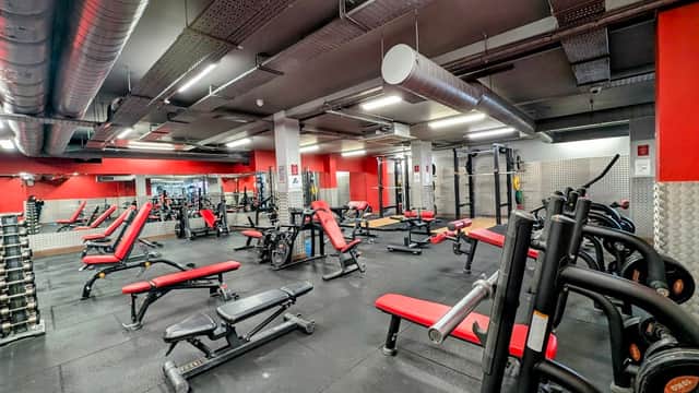 Modern gym interior with red and black equipment, weight benches, and various fitness machines in a spacious layout.