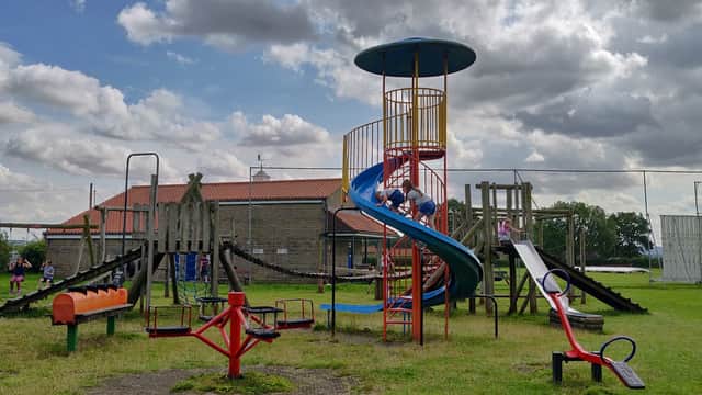 Colorful playground equipment, including slides and climbing structures, set on a grassy field under a cloudy sky.