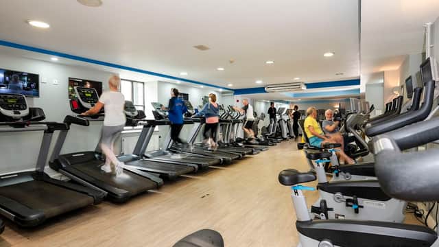 Fitness enthusiasts using treadmills and exercise bikes in a bright gym with modern equipment and large windows.